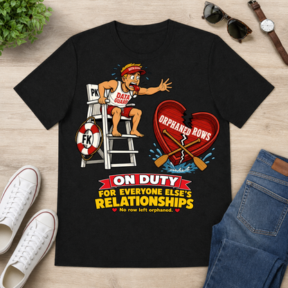 A black graphic t-shirt laid flat on a light wood surface, surrounded by lifestyle props including white sneakers, blue jeans, sunglasses, a watch, and a small plant. The t-shirt features a cartoon graphic of a lifeguard on a ladder next to a broken red heart with the text 'ORPHANED ROW' and the slogan 'ON DUTY FOR EVERYONE ELSE'S RELATIONSHIPS'.