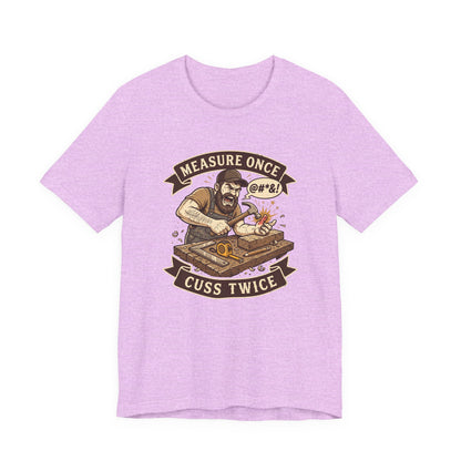 A light purple heather short-sleeve t-shirt with a graphic print of a bearded man playing a turntable, framed by banners reading 'MEASURE ONCE @#&1' and 'CUSS TWICE'.