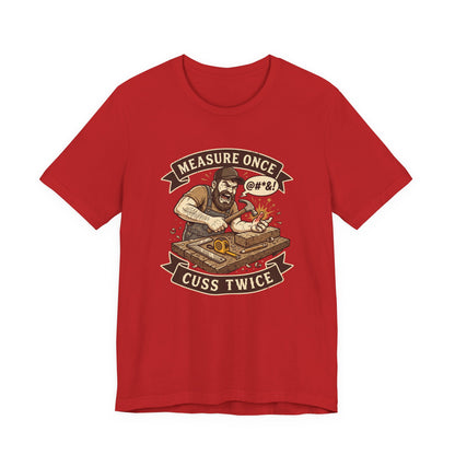 A red short-sleeve crewneck t-shirt featuring a vintage-style graphic of a bearded man measuring wood with a square and compass, surrounded by banners that read 'MEASURE ONCE' and 'CUSS TWICE'.